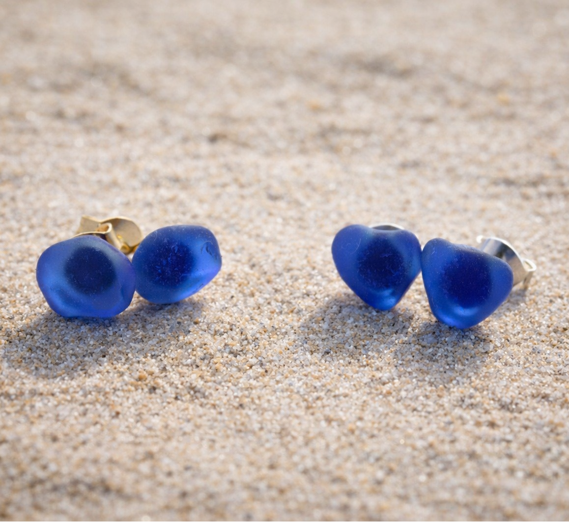cobalt beach glass stud earrings unique organic shapes ocean jewelry on a sandy surface